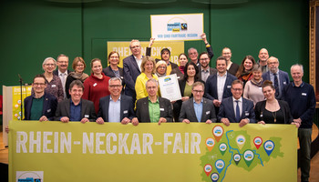 Wir sind Faire Region! | © VRRN / Schwerdt Menschen stehen hinter einem Banner von Rhein-Neckar Fair und lächeln. Hinten halten zwei Männer ein Schild hoch mit der Aufschrift: "Wir sind Faire Region" | © VRRN / Schwerdt